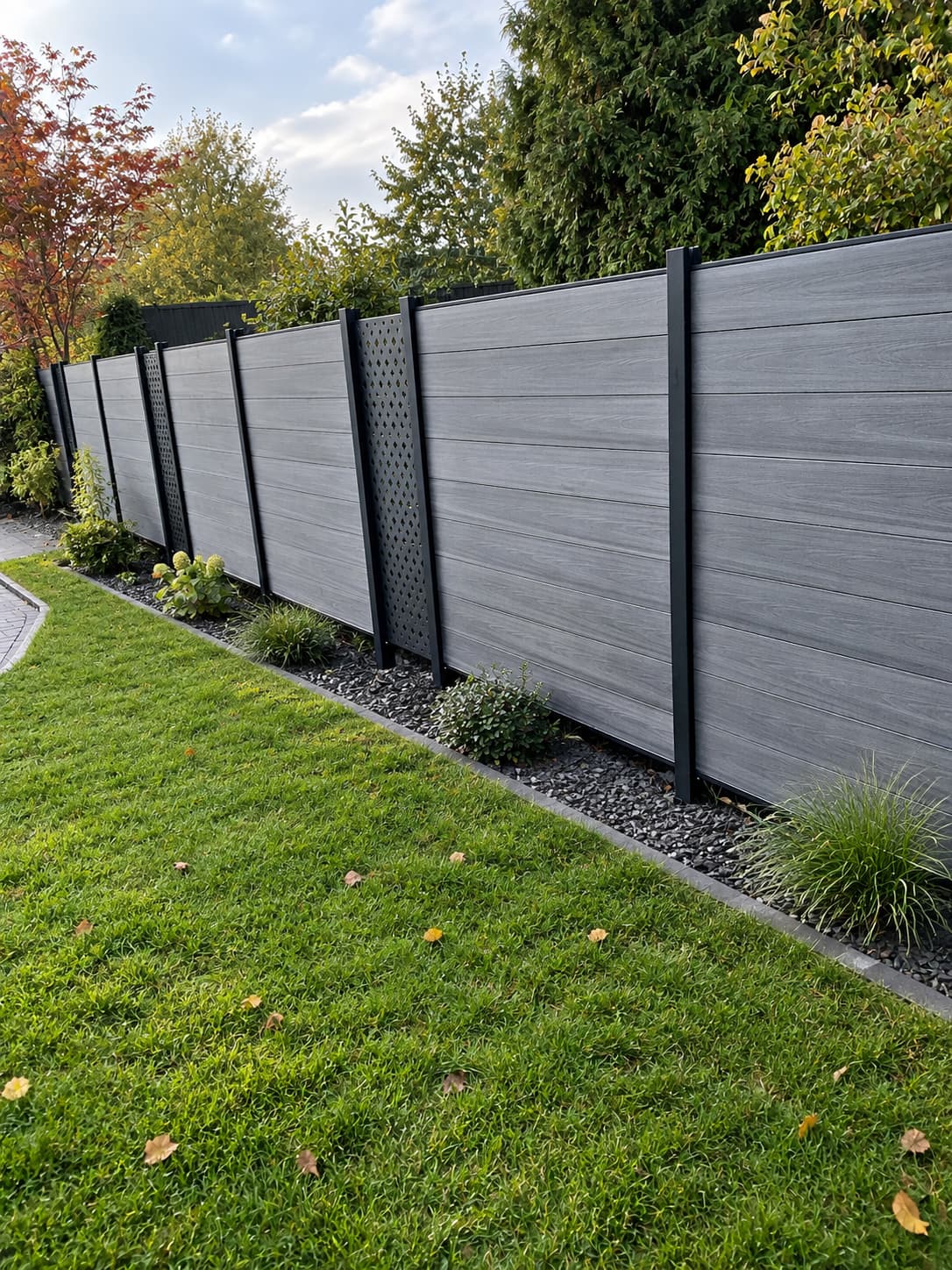 Grauer WPC-Zaun mit dunklen Pfosten und senkrechten Dekorelementen am bepflanzten Gartenrand