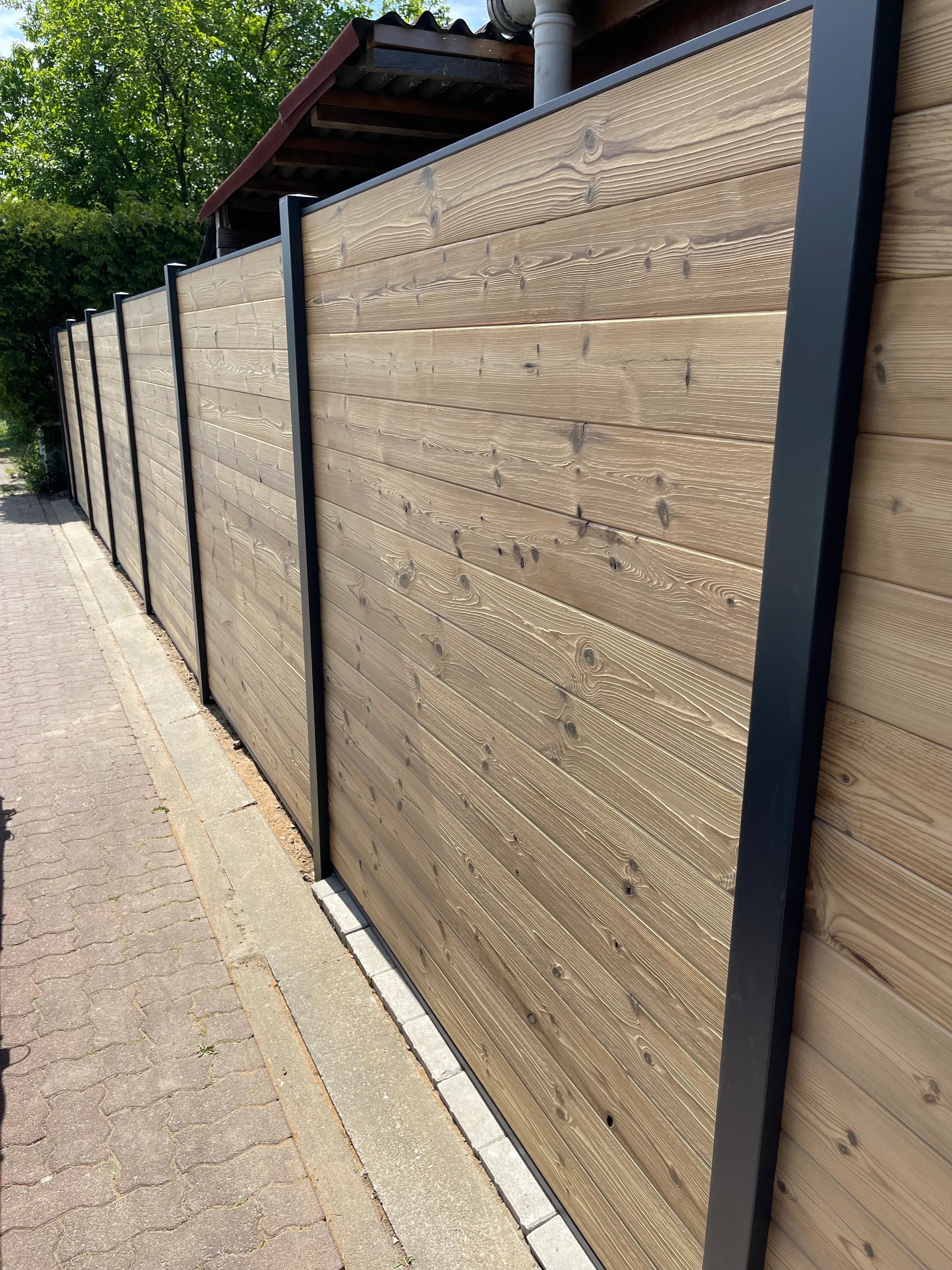 Sichtschutz mit ausgeprägter Holzmaserung und dunklen Pfosten entlang eines Weges