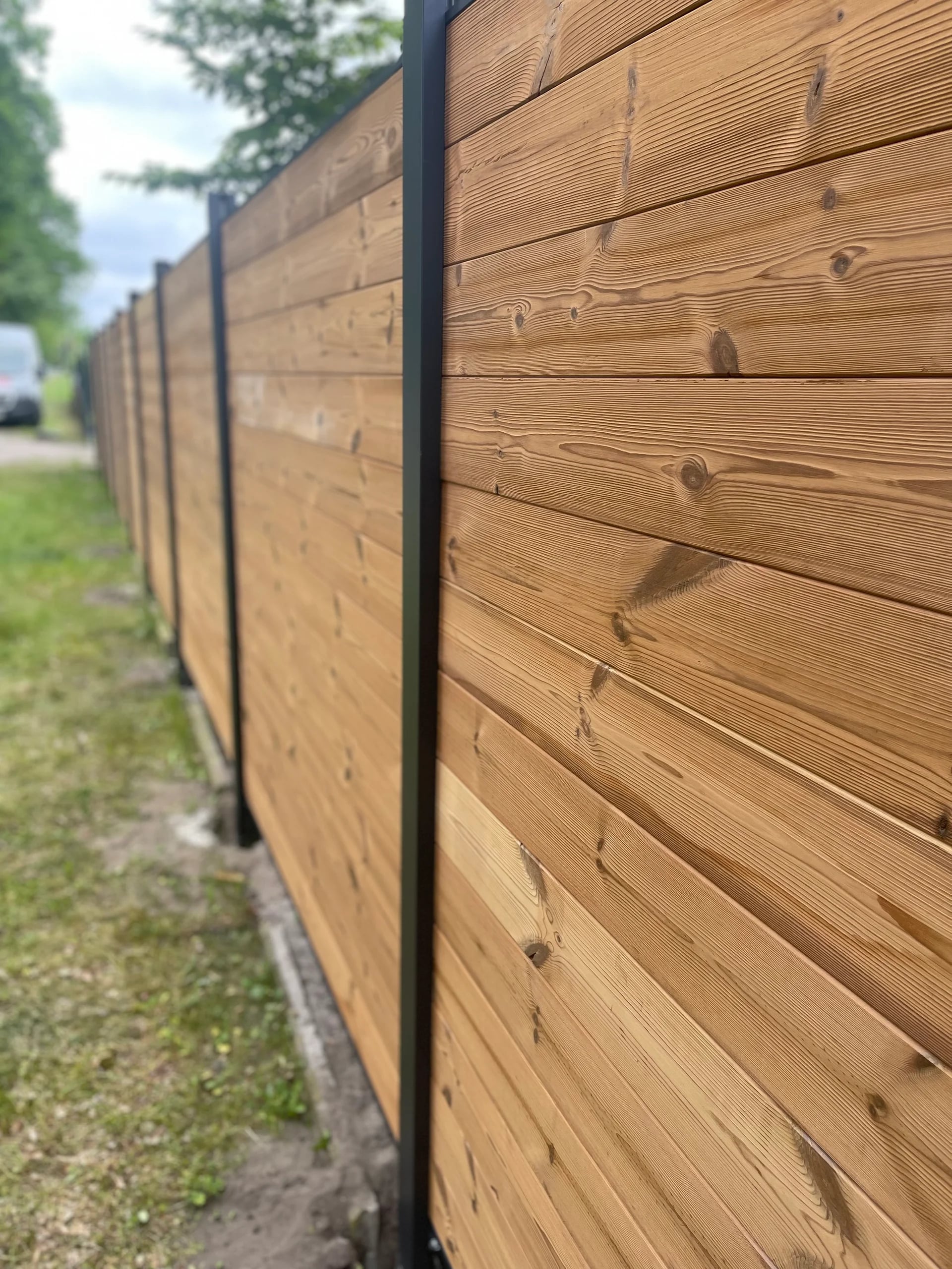 Holzzaun mit horizontalen Brettern, sichtbarer Maserung und dunklen Pfosten