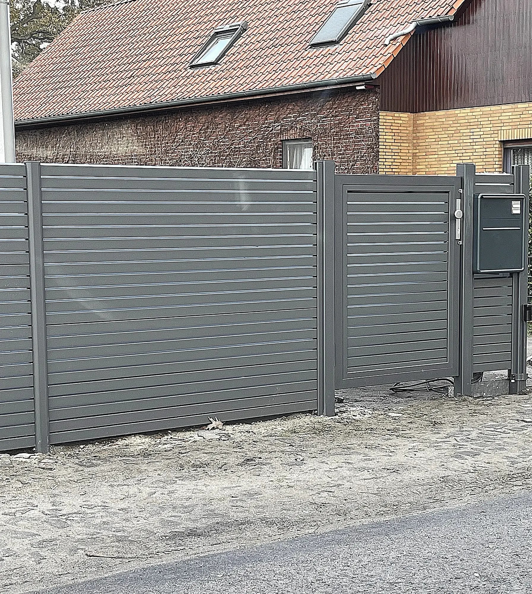 Aluminiumzaun und Tor mit integriertem Briefkasten vor einem Backsteinhaus